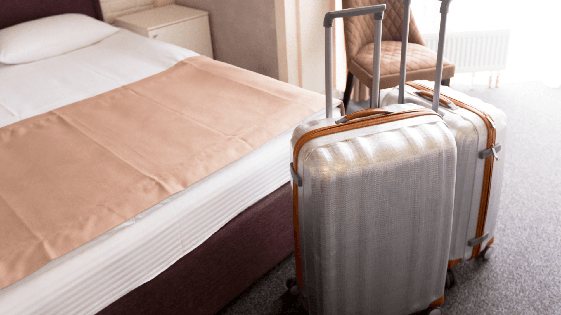Hard-shell luggage beside a hotel bed, helping prevent hotel bed bugs from hitching a ride.